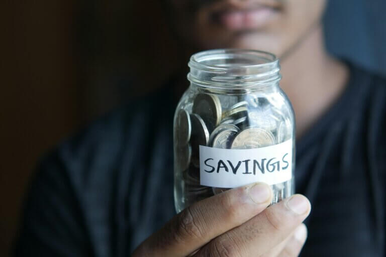 Person holding a jar with cash and coins labeled savings